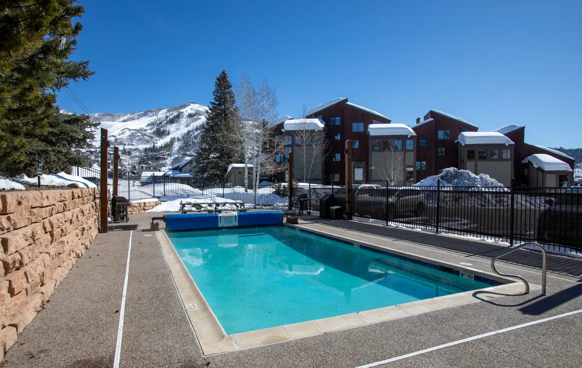A heated outdoor pool surrounded by snow and mountains, with winter sunlight glinting off the water. The contrast of the warm pool and snowy backdrop creates a unique and inviting winter resort scene.