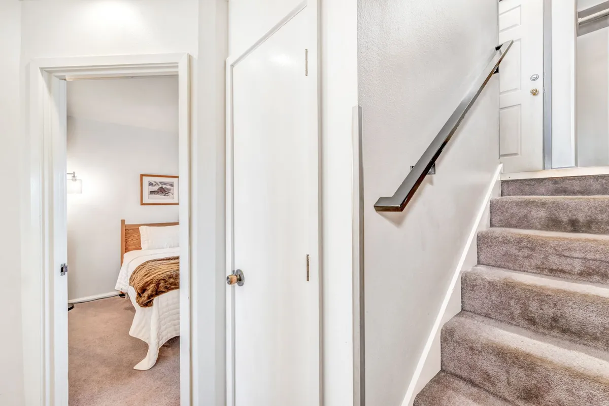 A cozy interior view showing a staircase leading up to a doorway where bedroom decor is visible, suggesting access to an additional private or semi-private retreat such as the loft area. The scene evokes a sense of separation and privacy within the home.