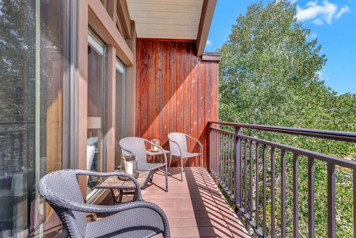 A tranquil balcony scene featuring cozy seating against a wooden wall, surrounded by trees. The balcony offers an inviting spot for intimate conversations, morning coffee, or stargazing, with the outdoors close at hand and a palpable sense of privacy.