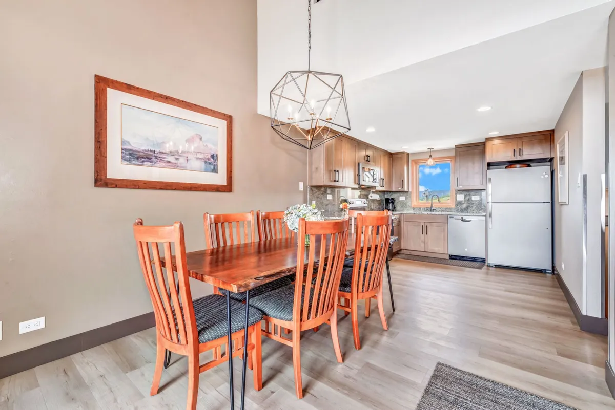 This photo captures an open-plan kitchen and adjacent dining area. The dining table is set for a group, and contemporary lighting creates a cozy, inviting ambiance. The kitchen area is visible in the background, suggesting seamless flow between cooking and communal dining.