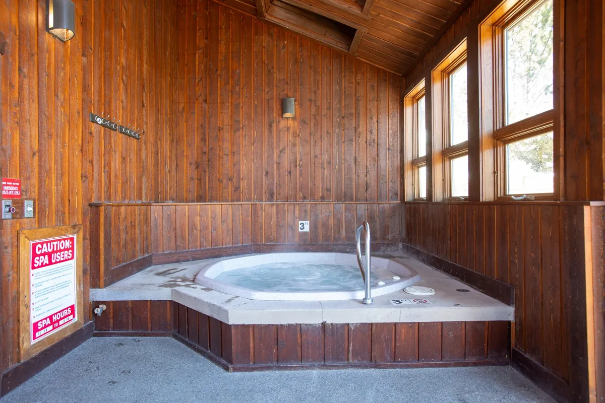 An inviting indoor hot tub surrounded by wood paneling and large windows, allowing natural light to pour in. The tranquil space is designed for relaxation, with soothing water and a cozy retreat ambiance inviting guests to unwind after a day of adventure.