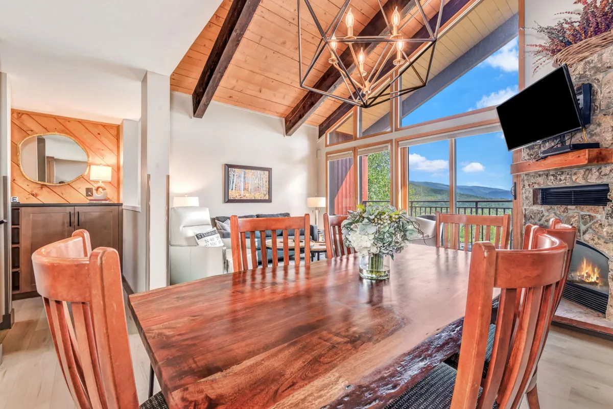 The space features a stylish dining area with a central table and chandelier, a fireplace, and large windows framing the mountain vista. The layout invites group dining, celebrations, and seamless flow between dining and living spaces, echoing the section’s emphasis on communal experiences.