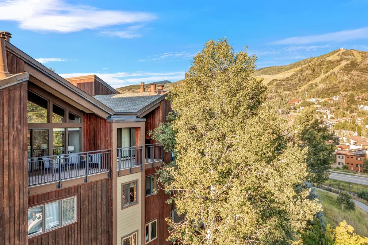 An exterior shot of a wooden balcony framed by mountain scenery and surrounded by trees. The balcony features sturdy railings and plenty of space for small gatherings, making it an ideal spot to take in sunset views, stargaze, or enjoy festival energy below.