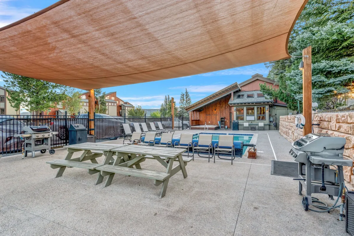 A casual outdoor space with a swimming pool, picnic table, barbecue grill, and several lounge chairs arranged for both sunbathing and socializing. The atmosphere is relaxed, hinting at both quiet moments and lively group activities by the pool.