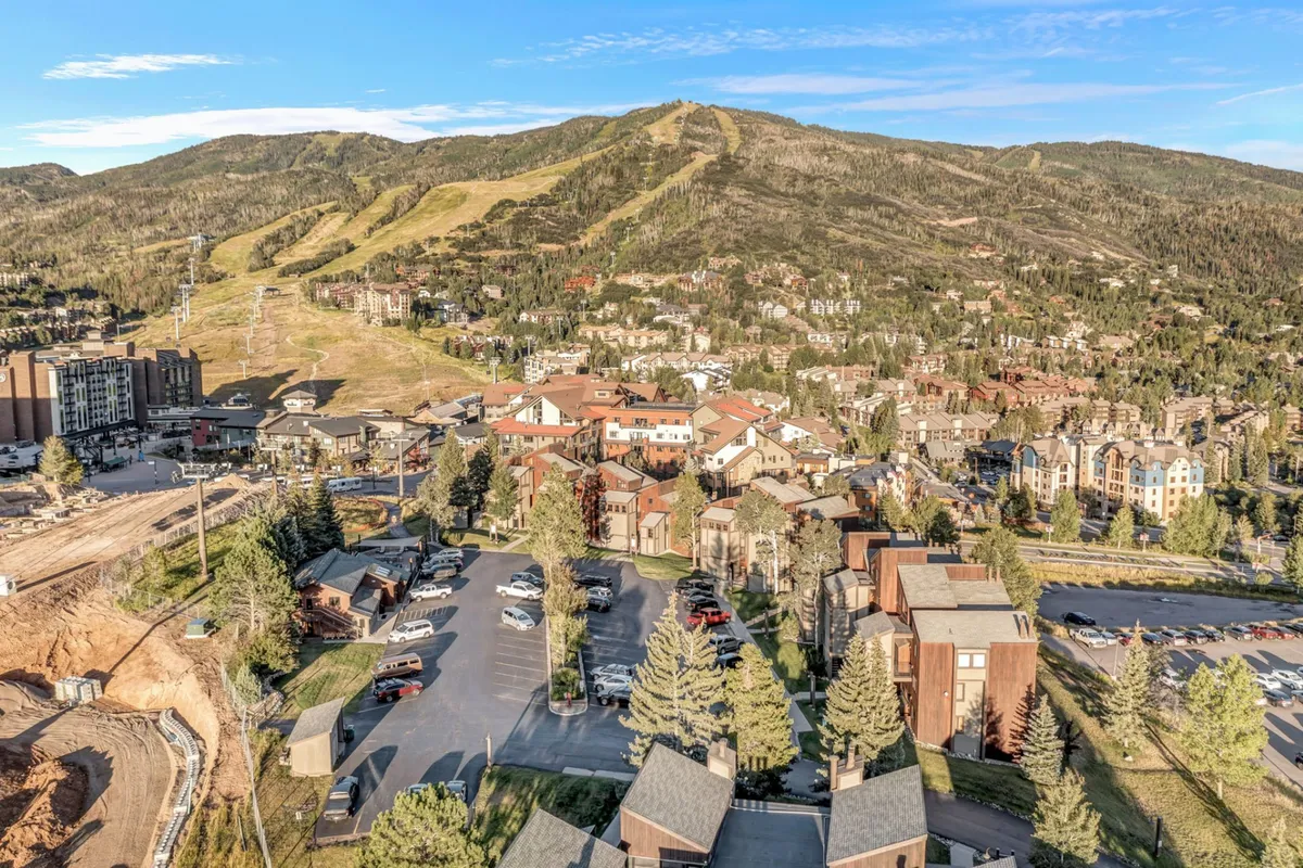 This exterior shot features a mountain backdrop, residential buildings, a parking area, and trees, capturing both the natural beauty and community atmosphere of the neighborhood.