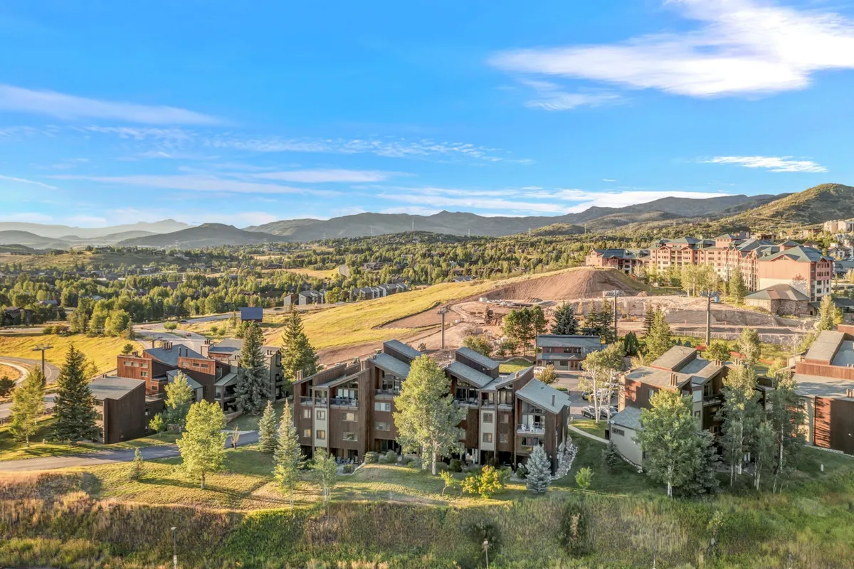 A wide exterior vista capturing a mountain range set against lush forest greenery and modern buildings under a clear blue sky. The scene evokes the allure of nearby trails and the natural surroundings that invite exploration and adventure.