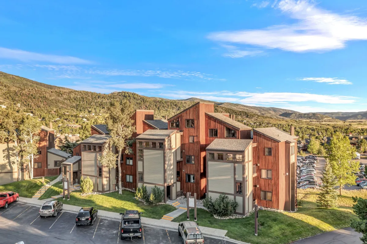 A contemporary building with balconies set amidst lush greenery and dramatic mountain backdrops. The architecture is modern yet blends seamlessly into the natural landscape, and the setting sun casts a warm glow over the scene. The balconies suggest private spaces ideal for morning coffee or sunset views, evoking a sense of serenity and connection to nature.