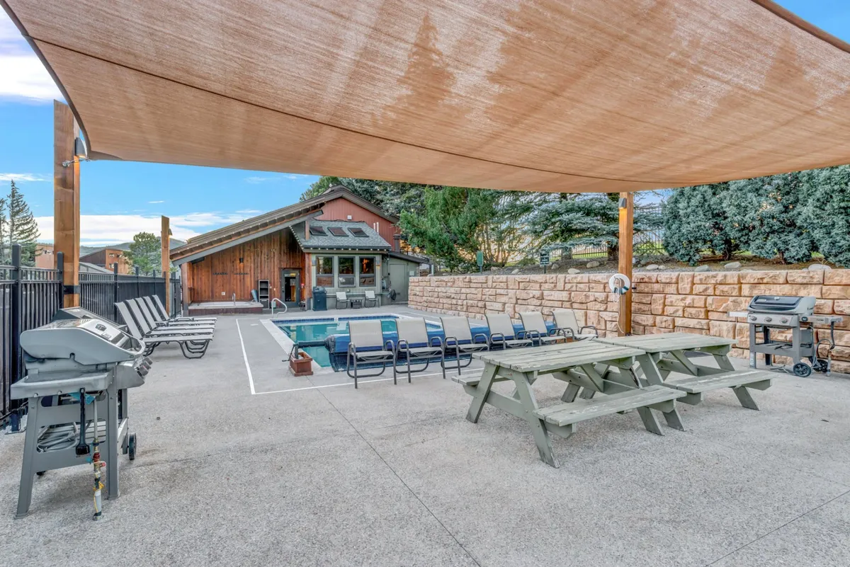 This scene captures a lively, shared outdoor space with a swimming pool, dining table, outdoor seating, grill, and shade canopy, set up for both barbecuing and socializing. The area feels casual and welcoming, perfect for summer gatherings or informal meetups.