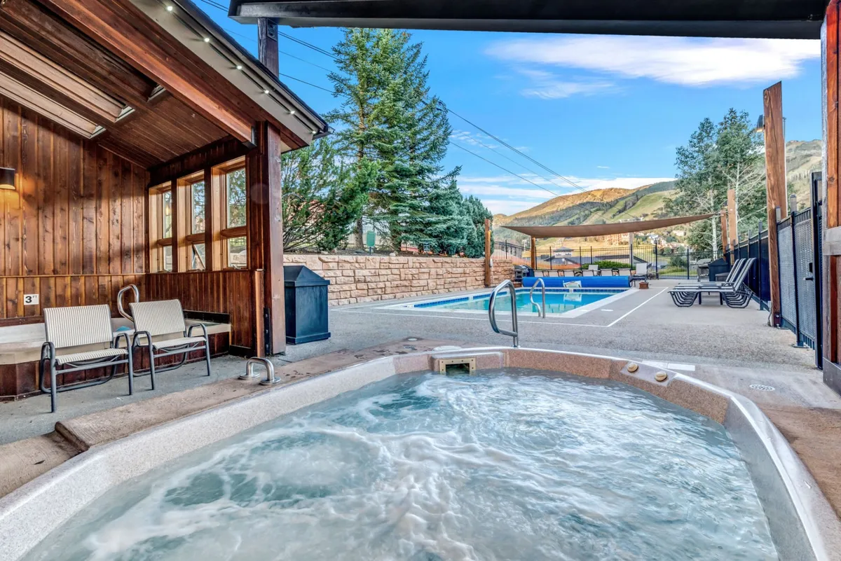 This image features a heated swimming pool and hot tub set against a stunning mountain backdrop, with a wooden structure nearby. Lounge chairs are arrayed around the pool area, inviting relaxation and socializing, while the mountains in the distance reinforce the resort vibe.