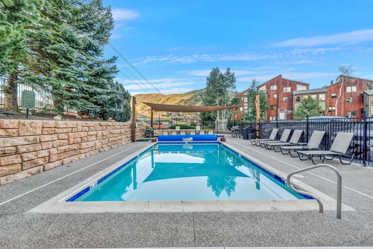 A vibrant outdoor pool area with lounge chairs and beautifully maintained landscaping, set against an impressive mountain backdrop. The pool is inviting, with space for groups to gather, swim, or relax together, and the mountain view hints at the proximity to adventure.